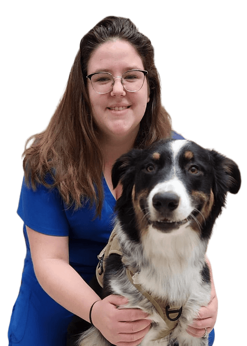 Female with long brown hair wearing glasses and blue scrubs posing with an Australian Shepherd